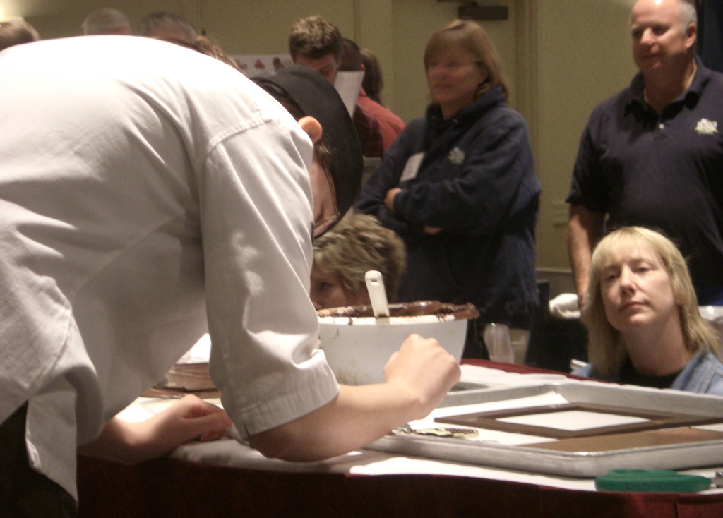 Eine Gruppe von Menschen vor einem Tisch mit einem Löffel, einer Schüssel und einem Tablett darauf, mit einer Bibel und einer Wand im Hintergrund.
