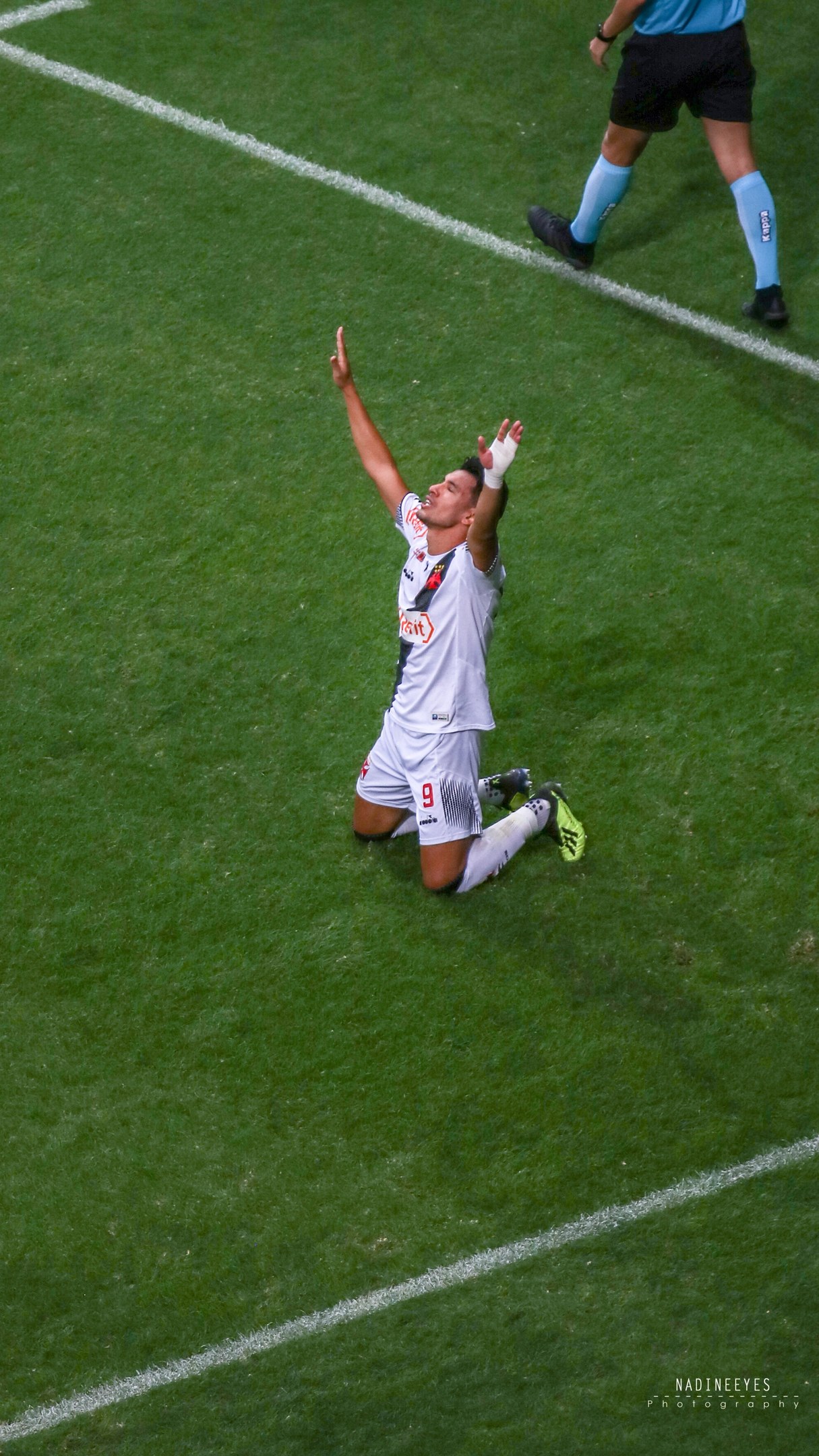 Ein Fussballspieler in einem Sportoutfit kniet auf dem Boden und streckt die Arme aus.