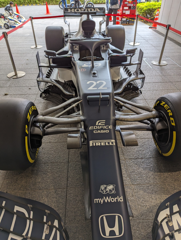 Ein McLaren Mercedes MP4-23 Formel-1-Rennwagen bei der Singapore Grand Prix, umgeben von Barrieren, Verkehrskegeln, Menschen, Fahrzeugen, Pflanzen, Bäumen und einem Gebäude im Hintergrund.