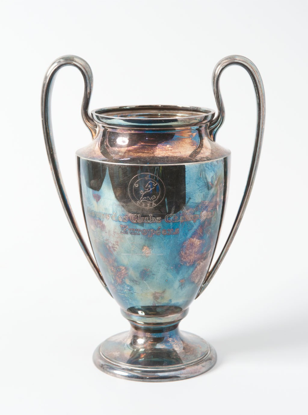 Der UEFA-Champions-League-Pokal, ein stahlerner Becher mit zwei Griffen und einem blauen und silbernen Farbschema, mit der Aufschrift "UEFA Champions League", vor einem weißen Hintergrund.