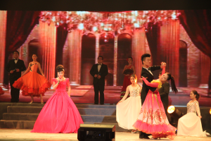 Eine Gruppe von Menschen auf einer Bühne mit Scheinwerfern, Stufen und einem Hintergrundbild, mit einem Lautsprecher unten, was eine Tanzvorführung vermuten lässt.