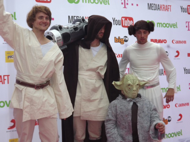 Gruppe von Menschen in Star-Wars-Kostümen, die auf einem roten Teppich posen und im Hintergrund ein Banner mit Text und Logos zu sehen ist.