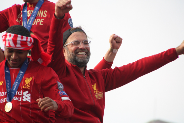 Liverpool-Trainer Jürgen Klopp feiert mit Spielern und Staff nach dem Gewinn der UEFA Champions League, trägt eine rote Jacke und hat zwei Medaillengewinner neben sich unter einem sichtbaren Himmel.