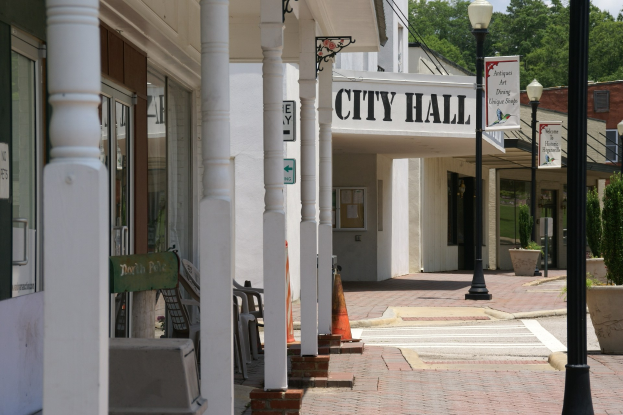 Stadtverwaltung mit umliegenden Gebäuden, Straßeninfrastruktur, Fahrzeugen und Vegetation unter einem bewölkten Himmel.