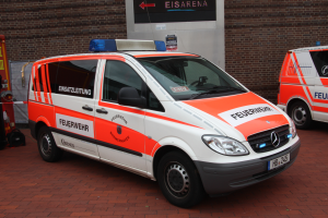 Zwei Rettungswagen nebeneinander vor einem Gebäude geparkt, mit einem Feuerlöscher und anderen Gegenständen auf der linken Seite des Bildes.