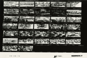 Schwarzes und weißes Foto einer vielseitigen Menge, die fröhlich um einen Fernseher versammelt ist, mit sichtbarem Text unten.