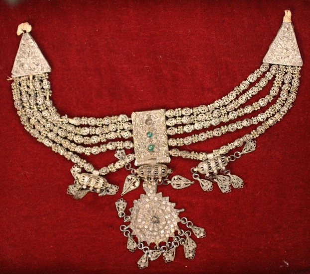 Silberne Kette mit Smaragden und Diamanten auf rotem Samt-Hintergrund.