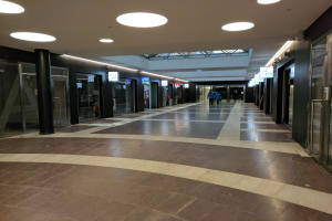 Langer Gang mit Menschen, Deckenlampen, Säulen, Glastüren und Informationsschildern, ähnlich einem belebten Rathaus.