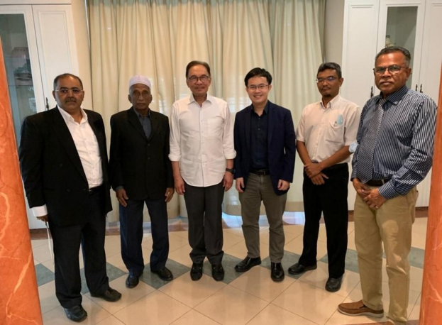 Eine Gruppe von Männern in einem formellen Raum mit zwei Säulen, Vorhängen und Schränken im Hintergrund, die sich unterhalten.