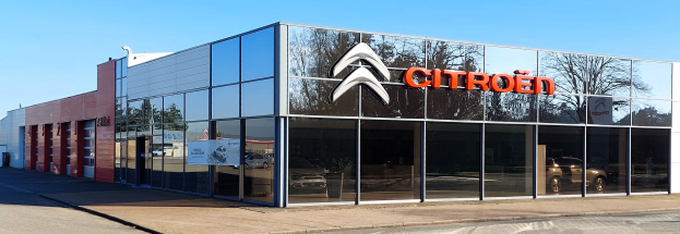 Außenansicht einer Citroën-Vertretung mit Glaswänden und -türen, einer Straße davor und einem klaren blauen Himmel.