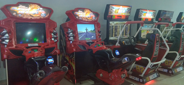 Eine Reihe buntfarbiger Arcade-Rennwagenautomaten auf einem Fliesenboden mit einer Wand im Hintergrund.