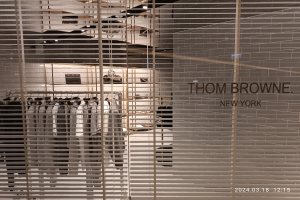 Ein Thomas Browne New York Flagship-Store-Interieur mit Kleidung an Bügeln, Wandtext, Deckenleuchten und diversen Gegenständen.