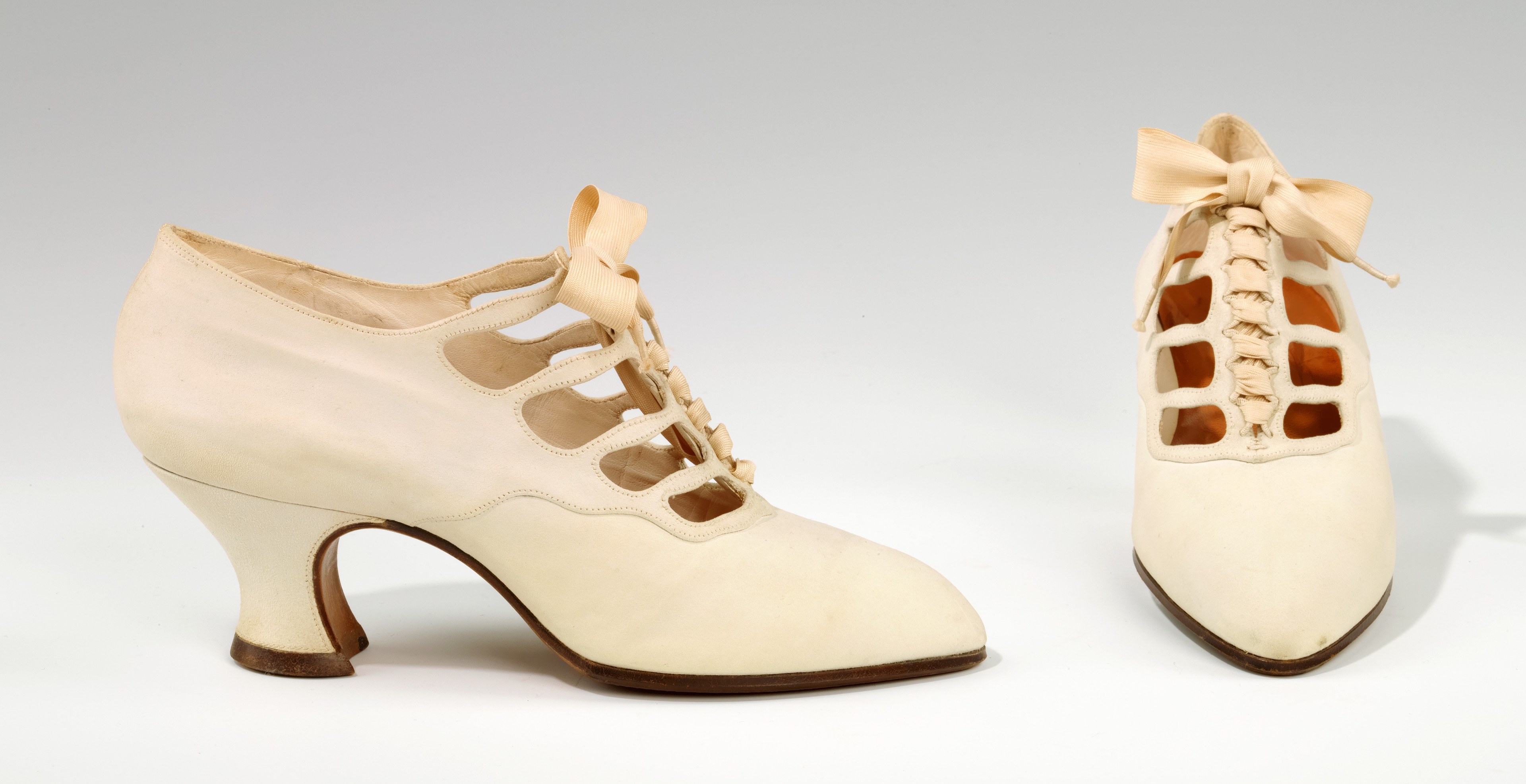 Weiße, spitz zulaufende, niedrige Absatzschuhe mit Schleife auf weißem Hintergrund.