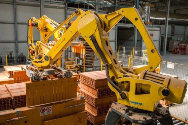 Großes Industriegebäude mit gestapelten Kisten, Kränen, Zaun, Strommasten und einer fernen Wand in einer automatisierten Fertigungsanlage.