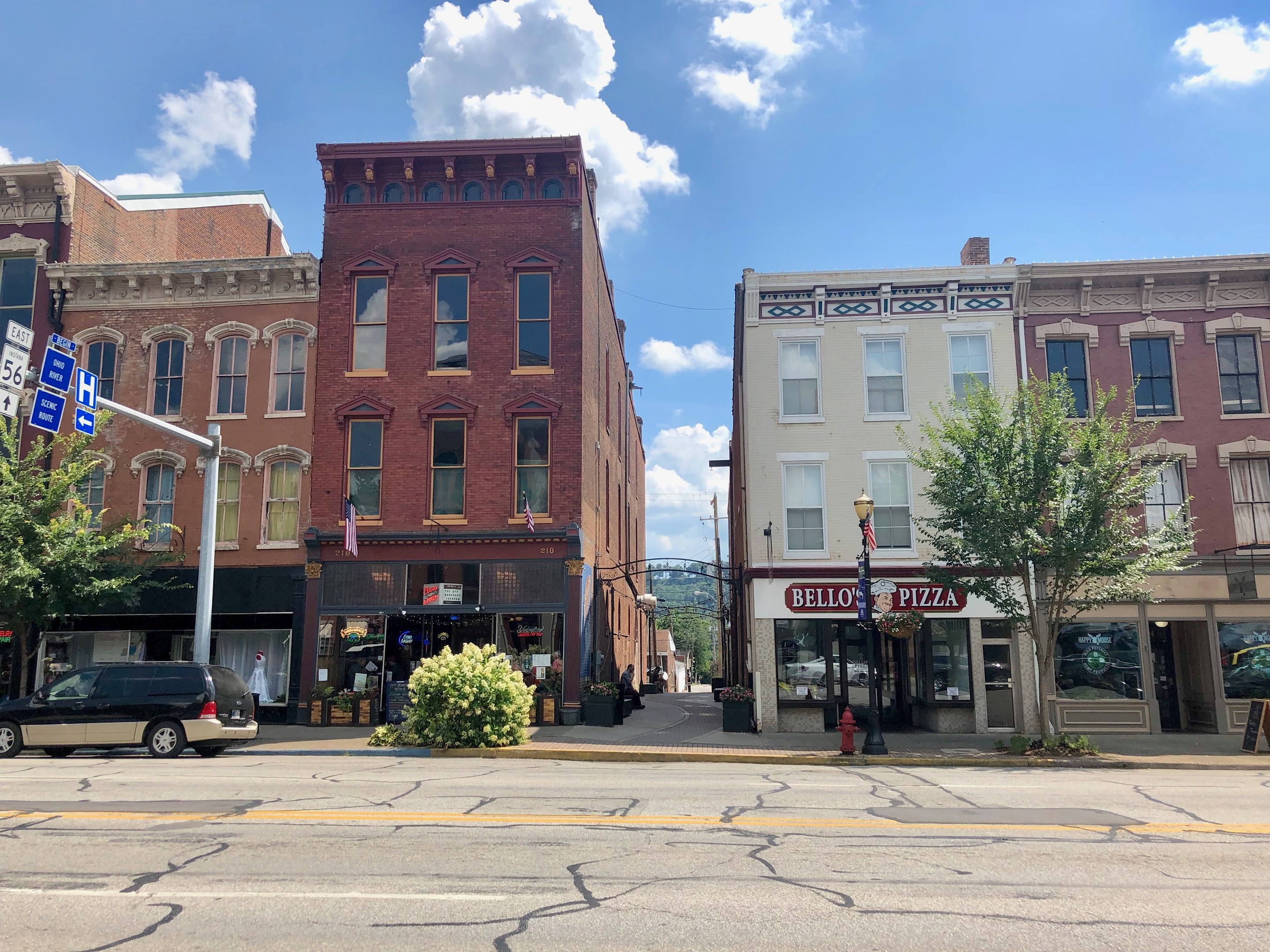 Eine Stra├če in der Stadt mit parkenden Autos, Geb├Ąuden, B├Ąumen, Laternen, Schildern und einem Feuerhydranten unter einem bew├Âlktem Himmel, die eine kommerzielle Immobilie repr├Ąsentiert.