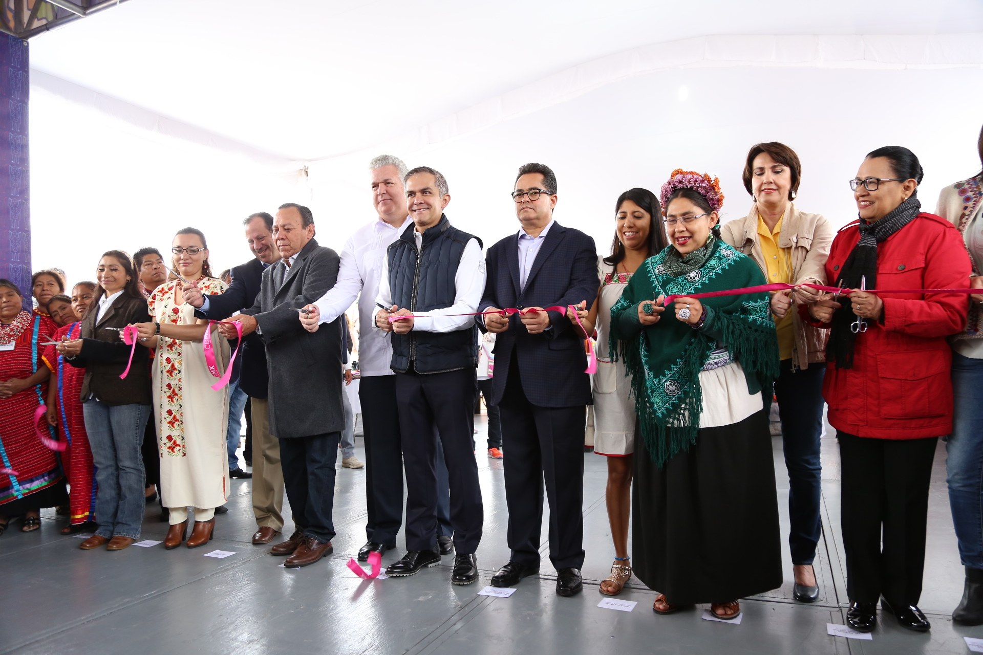 Eine Gruppe von Menschen, die mit Schere lächeln und vor einer Menge stehen, mit einer Säule links, verstreuten Papieren auf dem Boden und einem weißen Tuch im Hintergrund.