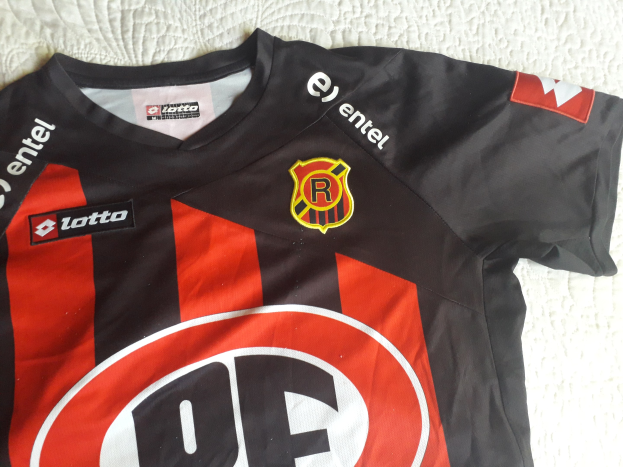 Schwarzer und roter Fussballjersey mit einem roten und schwarzen Streifen, mit einem Logo und Text, auf einer weissen Oberflache.