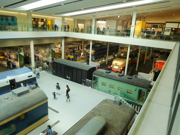 Ein großer Museumsraum mit verschiedenen Zugtypen, Informationsschildern, Geländern, Säulen und Beleuchtung.