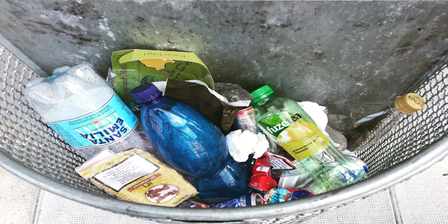 Ein Metallmüllcontainer voller Plastikflaschen, Tüten und diverser anderer Gegenstände.