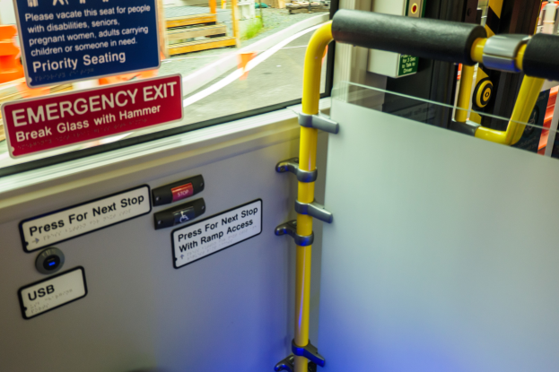 Notausgangsschild an der Seite eines Zuges mit einer Tür, Griff und einem Glasfenster, das die Straße, Pfosten und andere Objekte draußen zeigt.