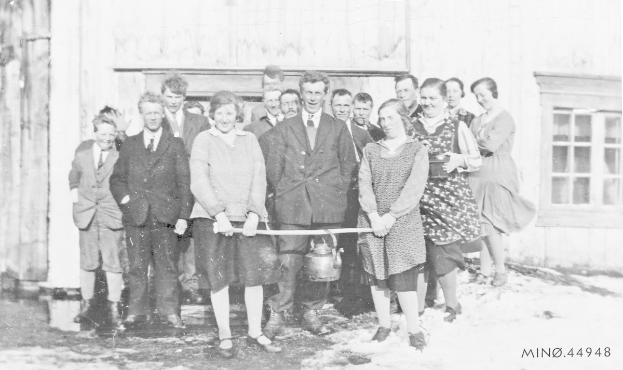 Schwarzes und weißes Foto einer Gruppe von Menschen, die strahlen und eine Schnur vor einem Gebäude mit einem Fenster und einer Tür halten, feiern die Eröffnung einer neuen Schule.