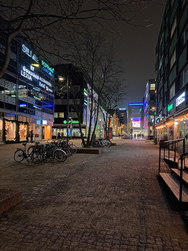 Eine nächtliche Straßenlaterne mit parkenden Fahrrädern, beleuchtet von Straßenlaternen, gesäumt von Bäumen und Gebäuden, mit Treppen mit Geländern, die zur Straße führen.