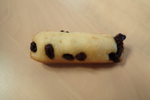 Ein Nahaufnahme eines goldbraunen Keks mit einer leichten Bestäubung von Puderzucker und Rosinen auf einem Holztisch.