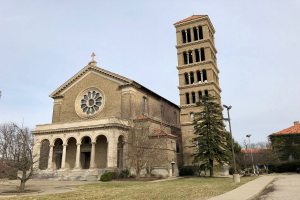 Die Basilika des Heiligen Herzens Jesu in St. Louis, Missouri, eine große Kirche mit einem zentralen Uhrturm, umgeben von Gebäuden, Straßenlaternen, Fahrzeugen, Bäumen und einem bewölkten Himmel.