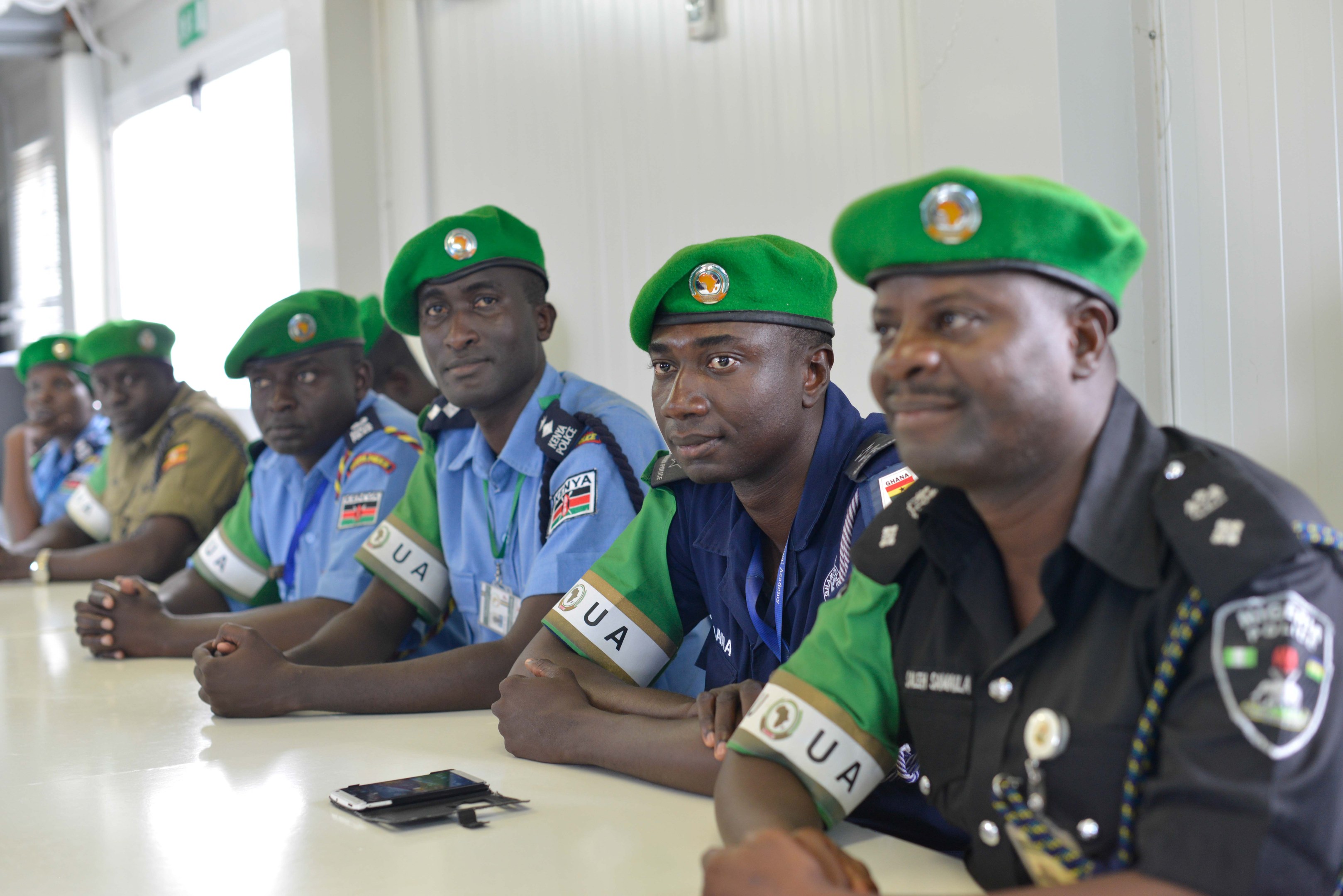 Gruppe von Polizisten bei einer Schulung am Tisch sitzend, mit Mobiltelefonen und anderen Gegenständen auf dem Tisch.