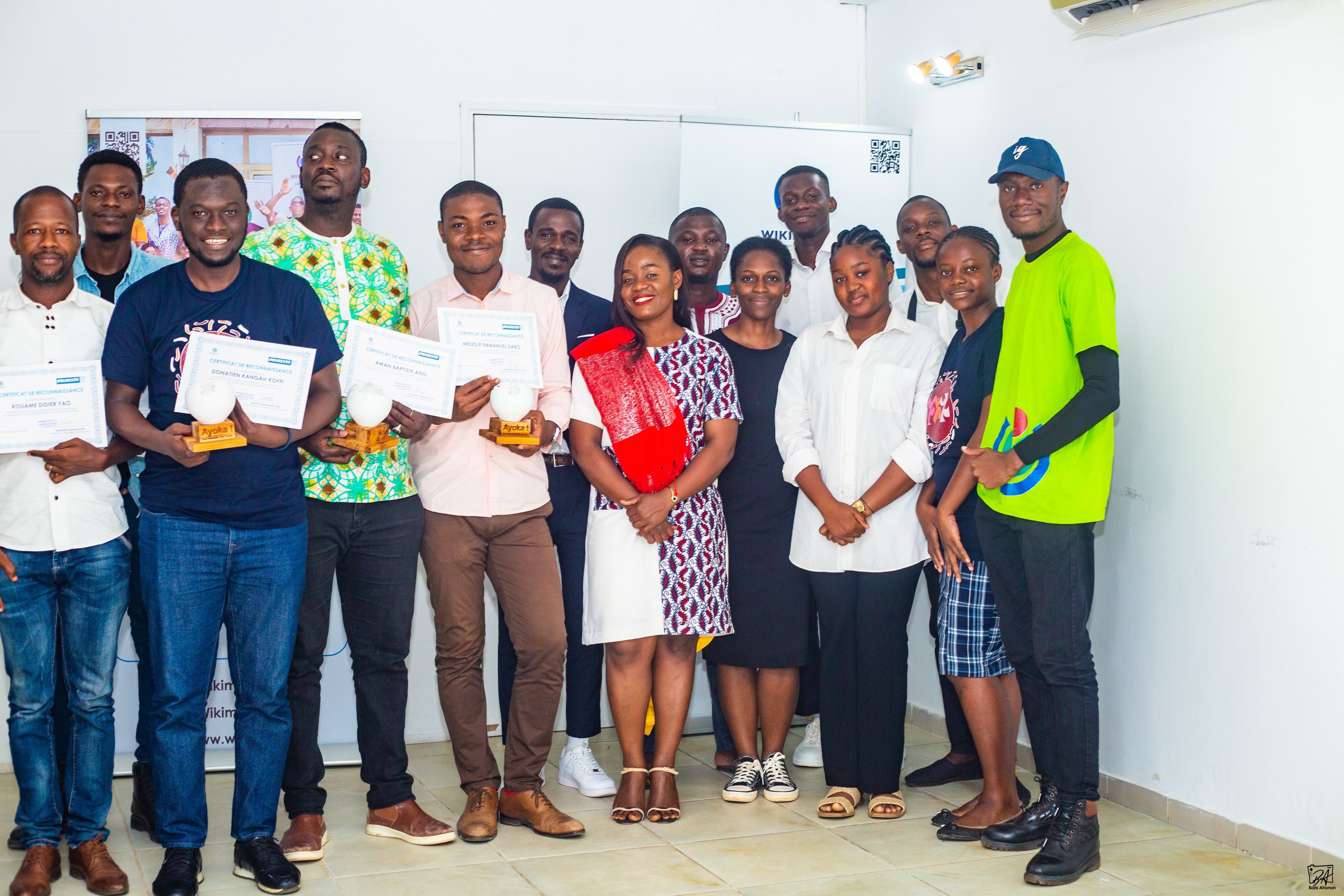 Eine Gruppe von Menschen, die strahlen und Zertifikate in einem Raum mit einer Klimaanlage, einer Whiteboard und einem Plakat halten, feiern die Einweihung einer neuen Schule in Nigeria.