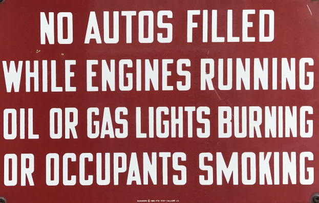 Ein rotes Schild mit weißer Schrift warnt davor, Autos während des Laufens des Motors, des Brennens von Öl oder Gas oder des Rauchens von Insassen aufzufüllen.