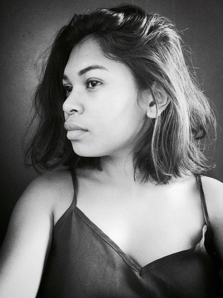 Eine selbstbewusste Frau in einem schwarzen Kleid posiert in einem Schwarz-Weiß-Foto vor einer Wand mit einem eleganten Bob und natürlichem Make-up.