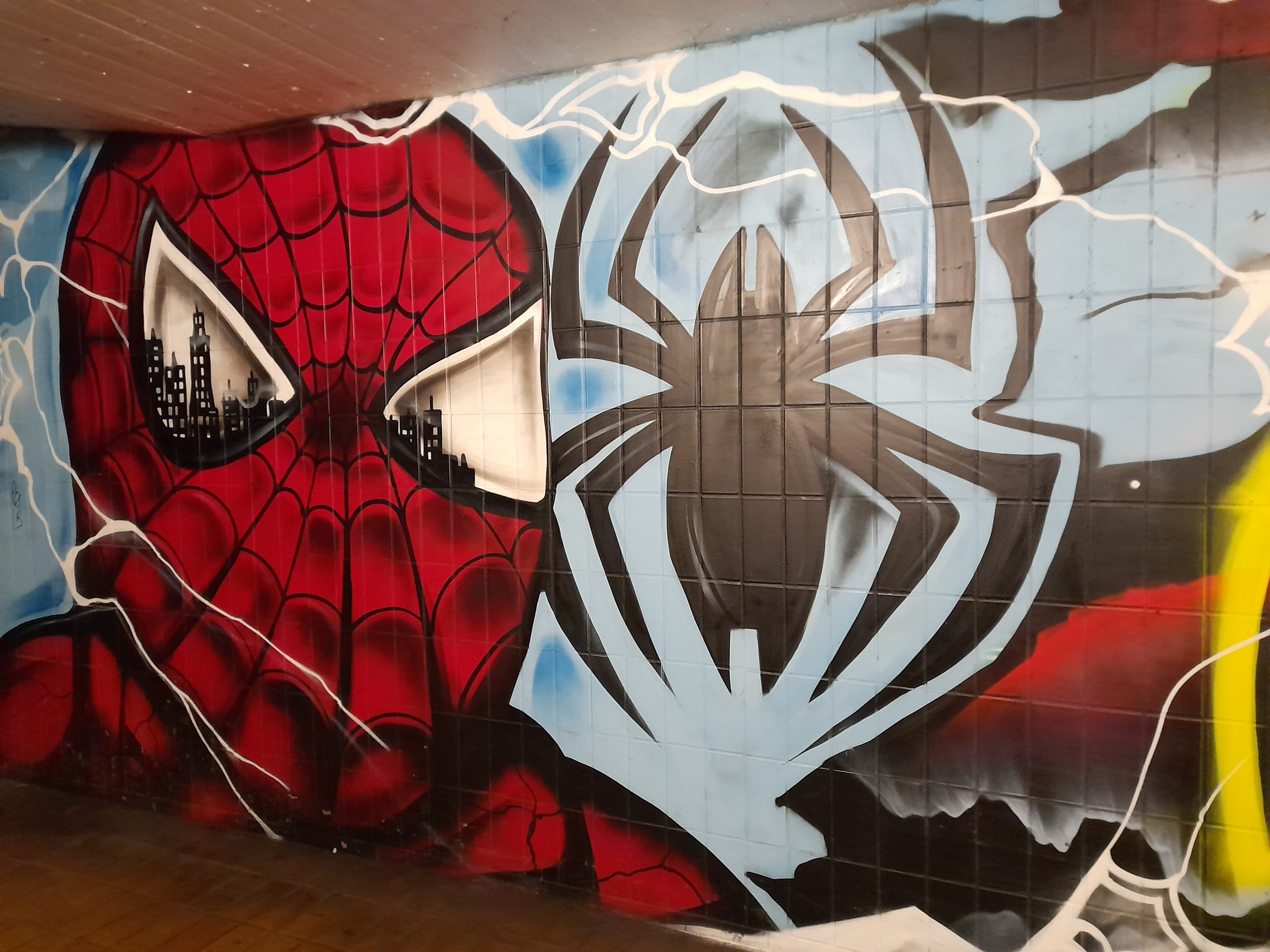 Buntes Wandgemälde von Spider-Man in rot und blauem Kostüm mit Webmuster und Spinnenlogo an der Seite eines Gebäudes.