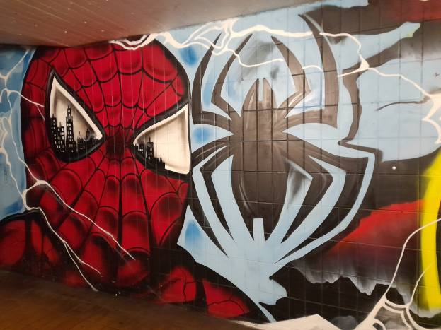 Buntes Wandgemälde von Spider-Man in rot und blauem Kostüm mit Webmuster und Spinnenlogo an der Seite eines Gebäudes.