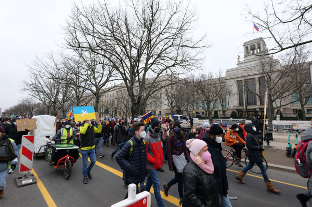 Eine große Gruppe von Menschen marschiert bei einer Demonstration auf einer Stadtstraße in Washington, D.C., mit Schildern und Transparenten, einige fahren Fahrräder, und Bäume und ein Gebäude im Hintergrund bei einem klaren blauen Himmel, Januar 21, 2020.