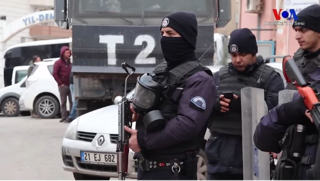 Eine Gruppe von Polizisten in Uniform steht zusammen auf einer Straße und hält Waffen während einer anti-regierungsamtlichen Demonstration in Ankara, Türkei, mit Fahrzeugen, Menschen, Gebäuden und Texttafeln im Hintergrund.