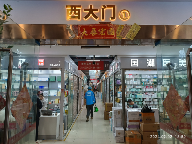 Innenraum einer chinesischen Apotheke mit Glaswänden, Regalen voller Artikel, verstreuten Kartons, einer Pflanze auf der linken Seite und einem Namensschild oben, das darauf hinweist, dass es sich um eine chinesische Drogerie handelt.