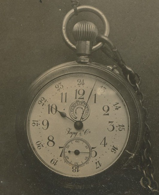 Ein Schwarz-Weiß-Foto einer antiken Taschenuhr mit einer Kette, die eine nummerierte Zifferblatt zeigt.