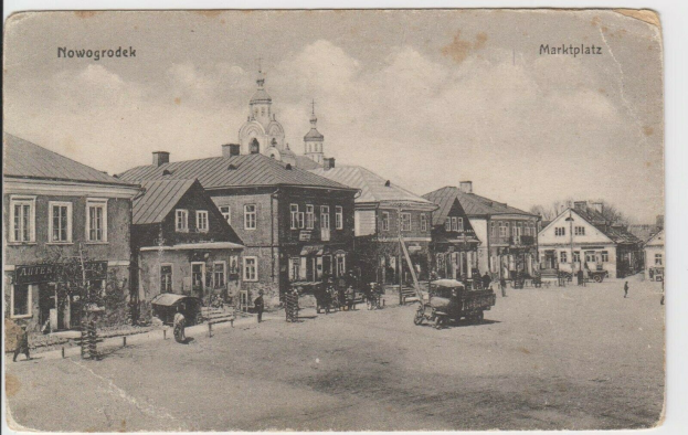 Schwarzer und weißer Fotograf einer Straße in Nowogrodziek, Deutschland, mit Gebäuden, Menschen, Wagen, Pfölen, Bäumen und Himmel, mit der Beschriftung "Marktplatz in Nowogrodeek, Deutschland" oben und unten.