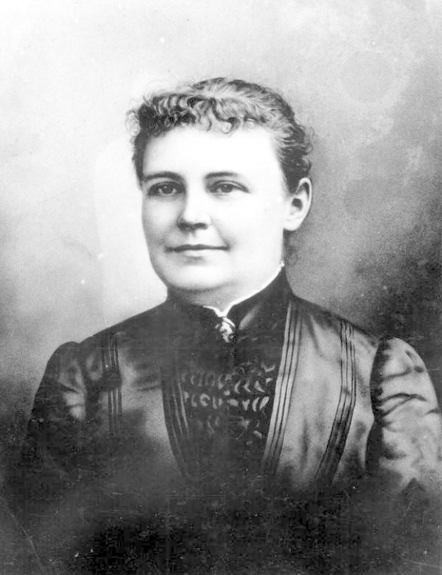 Schwarzes und weißes Foto einer Frau in einem Kleid, die mit gefalteten Händen und erhobenem Haupt steht und Entschlossenheit und Stärke ausstrahlt.