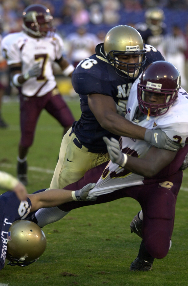 Zwei Fußballspieler in Sportkleidung und Helmen, einer hält den anderen auf dem Feld fest.