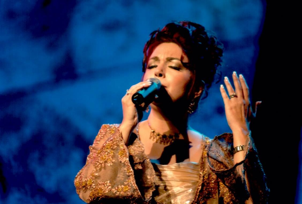 Eine Frau in einem goldenen Kleid singt auf der Bühne in ein Mikrofon vor einem blauen und schwarzen Hintergrund und tritt beim Eurovision Song Contest auf.