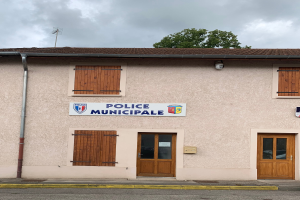 Ein Polizei-Gebäude mit einem Schild, Fenstern, Türen, einer Namensschilder, einem Rohr, einem Baum und einem bewölkten Himmel im Hintergrund.