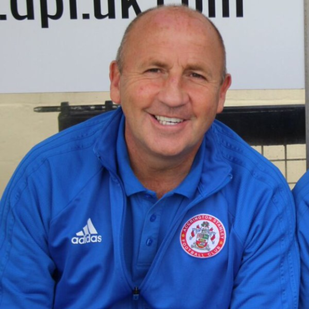 Zwei strahlende Männer in einem Raum, einer in einer blauen Jacke, wahrscheinlich der Trainer des Accrington Stanley Football Club, mit einer Tafel an der Wand dahinter.