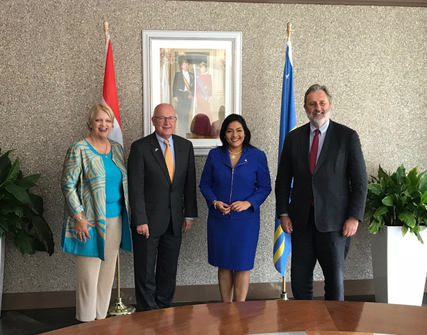 Eine Gruppe strahlender Menschen um einen Tisch mit Papieren herumstehend, umgeben von Flaggen, Topfpflanzen und einem Foto auf dem Wand, feiert die Unterzeichnung eines Memorandums von Verständnis zwischen den Vereinigten Staaten und Kanada.