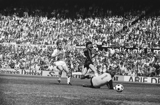 Schwarzes Foto von Fussballspielern im Einsatz auf einem Feld mit Zuschauern im Hintergrund und einer Bundesliga 1978-79 Ajax 1-1 Hannover 96-Banner.