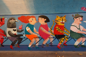 Mural an einer Gebäudeseite, das Menschen auf Fahrrädern zeigt, mit einer Straße darunter und Himmel darüber, Teil einer Londoner Street-Art-Serie.