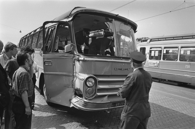 Schwarzes und weißes Bild eines verunglückten Busses auf einer Straße mit einer Gruppe von Menschen drumherum und anderen Fahrzeugen im Hintergrund.