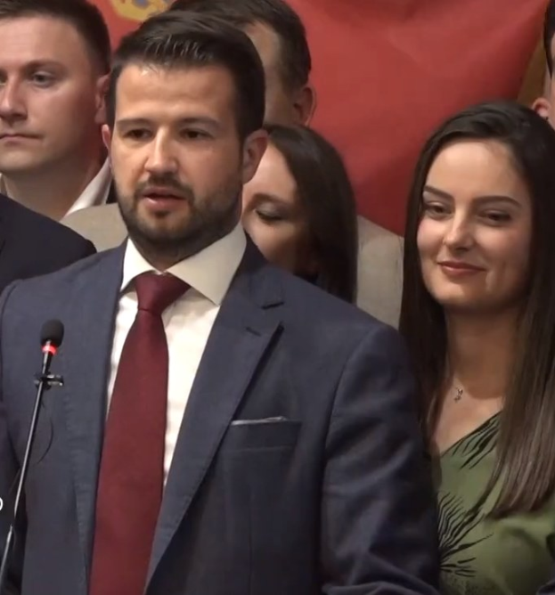 Ein Mann im Anzug spricht an einem Podium mit Mikrofon zu einer Menge hinter einem Banner, wahrscheinlich über ein Regierungverbot von Social Media.