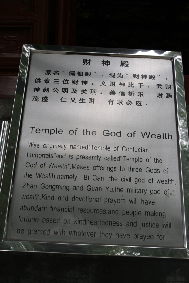 Ein Tempel, der dem Gott des Reichtums gewidmet ist, mit einer Namenschilder im Vordergrund und einer T├╝r im Hintergrund, umgeben von üppiger Vegetation.